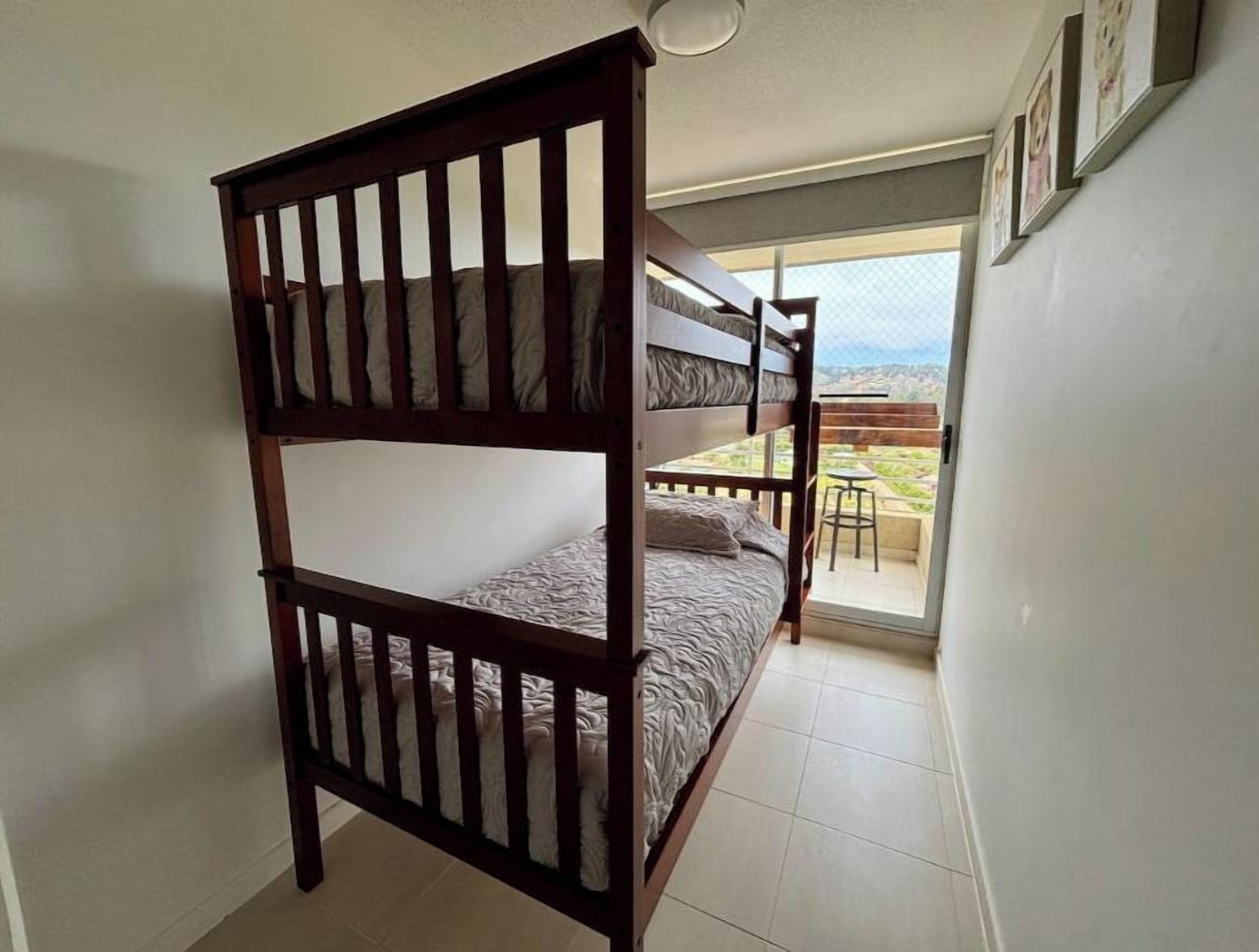 Habitación con literas y un taburete pequeño cerca de un ventanal corredizo que da a un balcón.