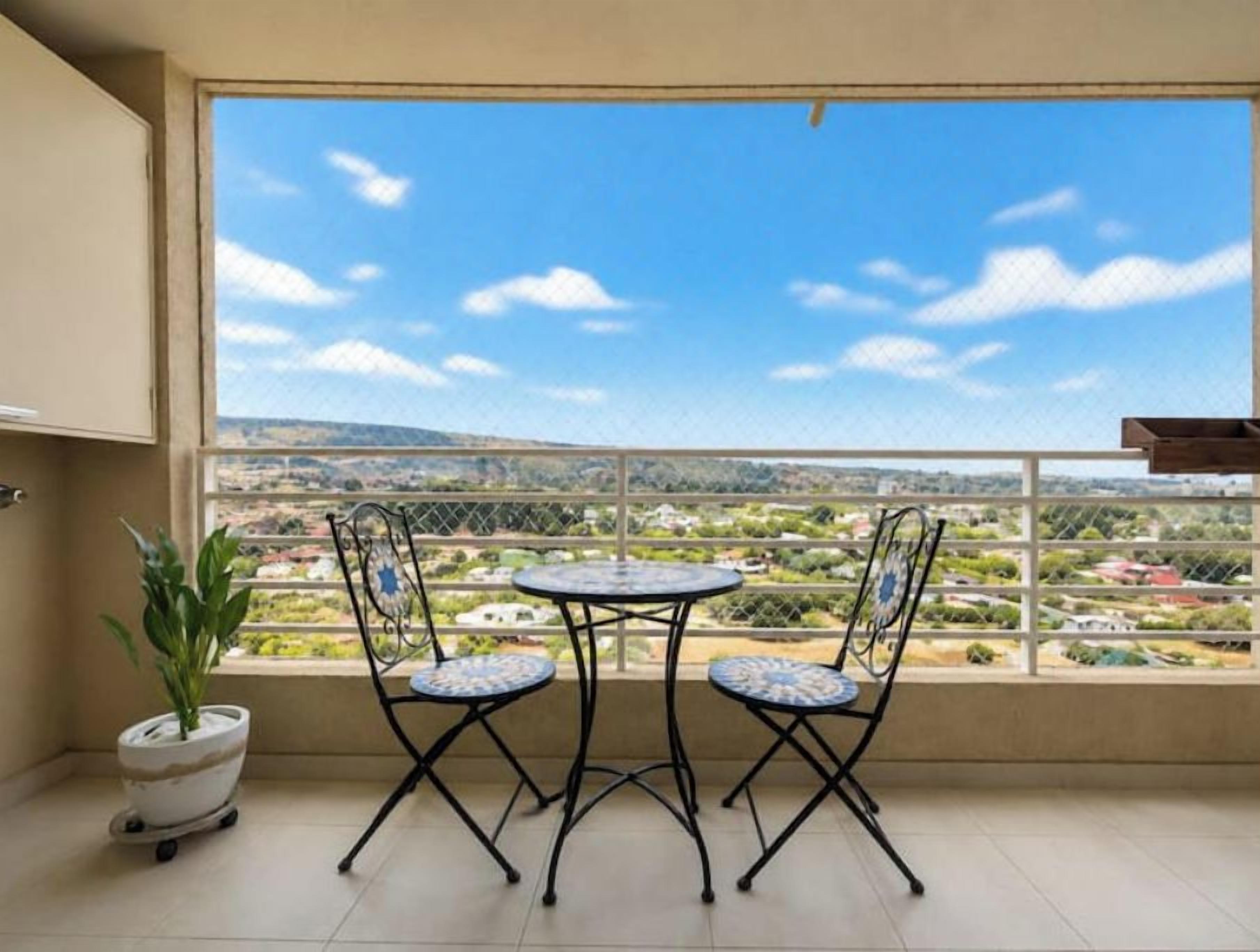 A balcony with a view of a cityscape, two chairs, and a potted plant.