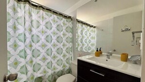 Un baño con inodoro, lavabo con espejo y cortina de ducha con diseño geométrico.