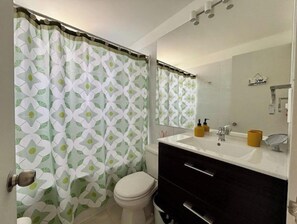Ein Badezimmer mit Toilette, Waschbecken mit Spiegel und einer Duschkabine mit geometrischem Muster.