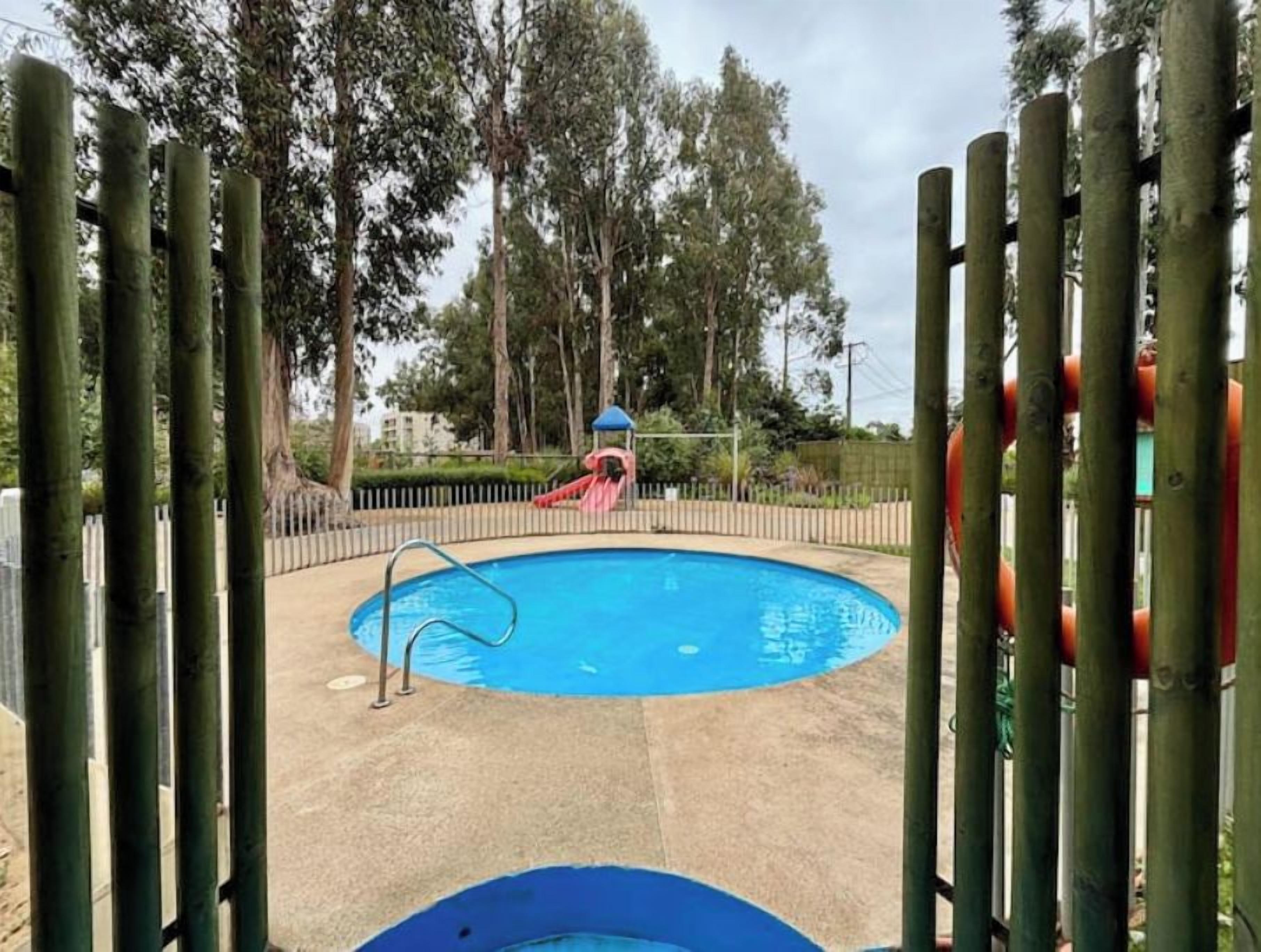 Una piscina con tobogán, rodeada por una valla y árboles.