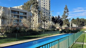 Una piscina con valla verde, rodeada de árboles y edificios.