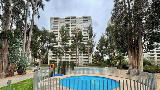 Zona residencial con piscina rodeada de vallas, árboles y un edificio alto al fondo.