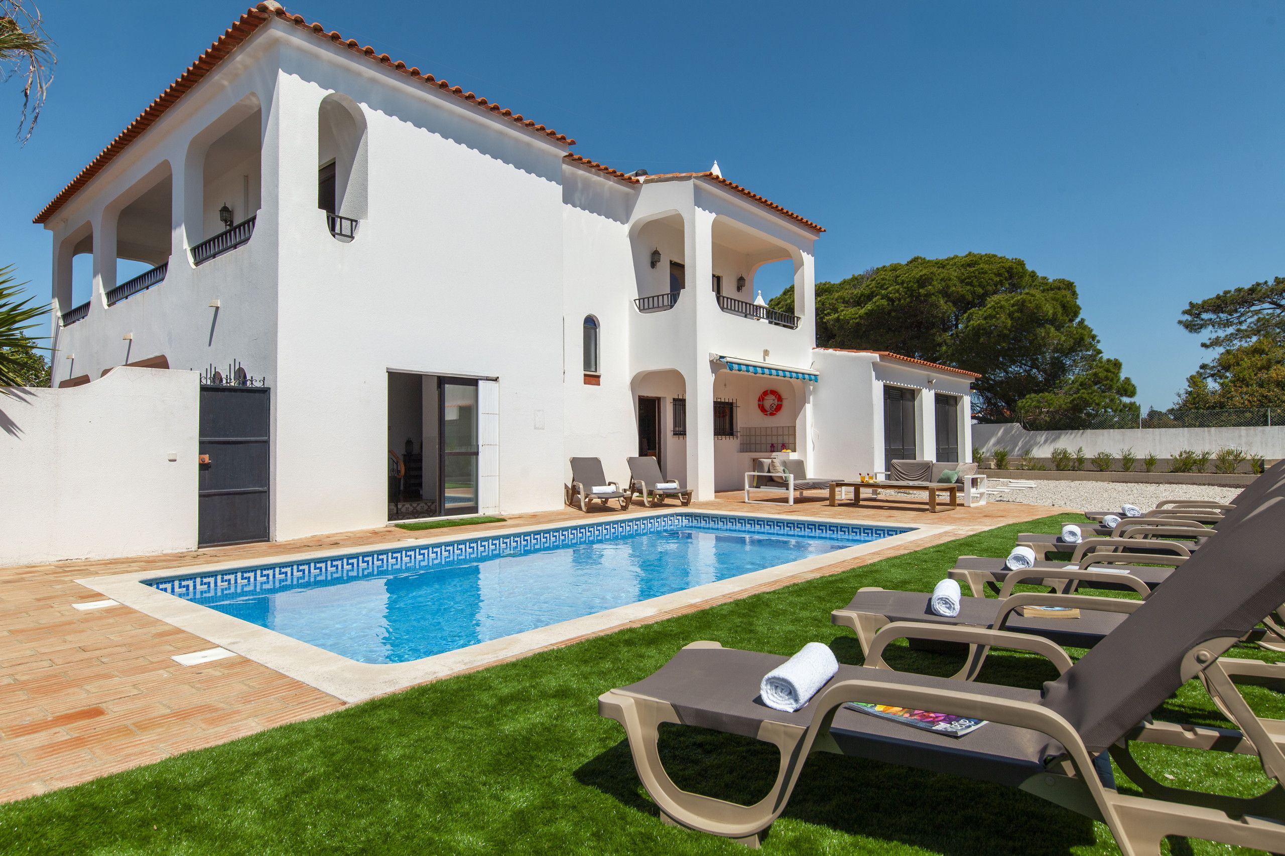 A white villa with a swimming pool, outdoor seating, and a well-maintained lawn.