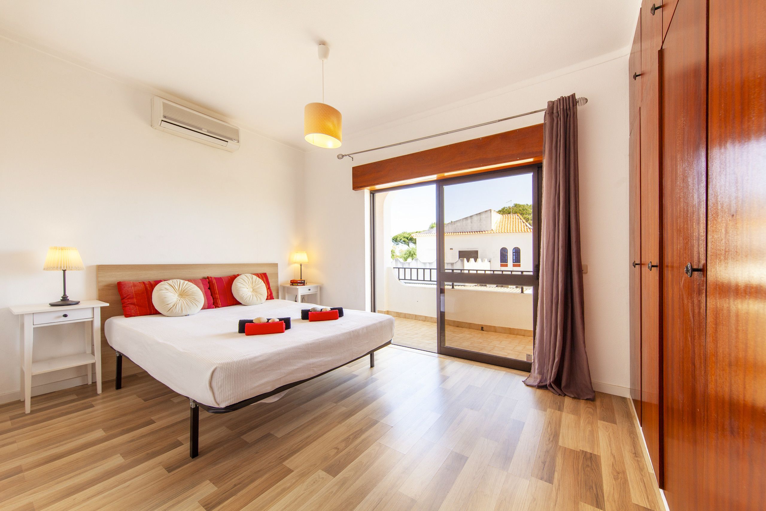 A modern bedroom with a large bed, bedside tables, a ceiling fan, and a view to the outside.