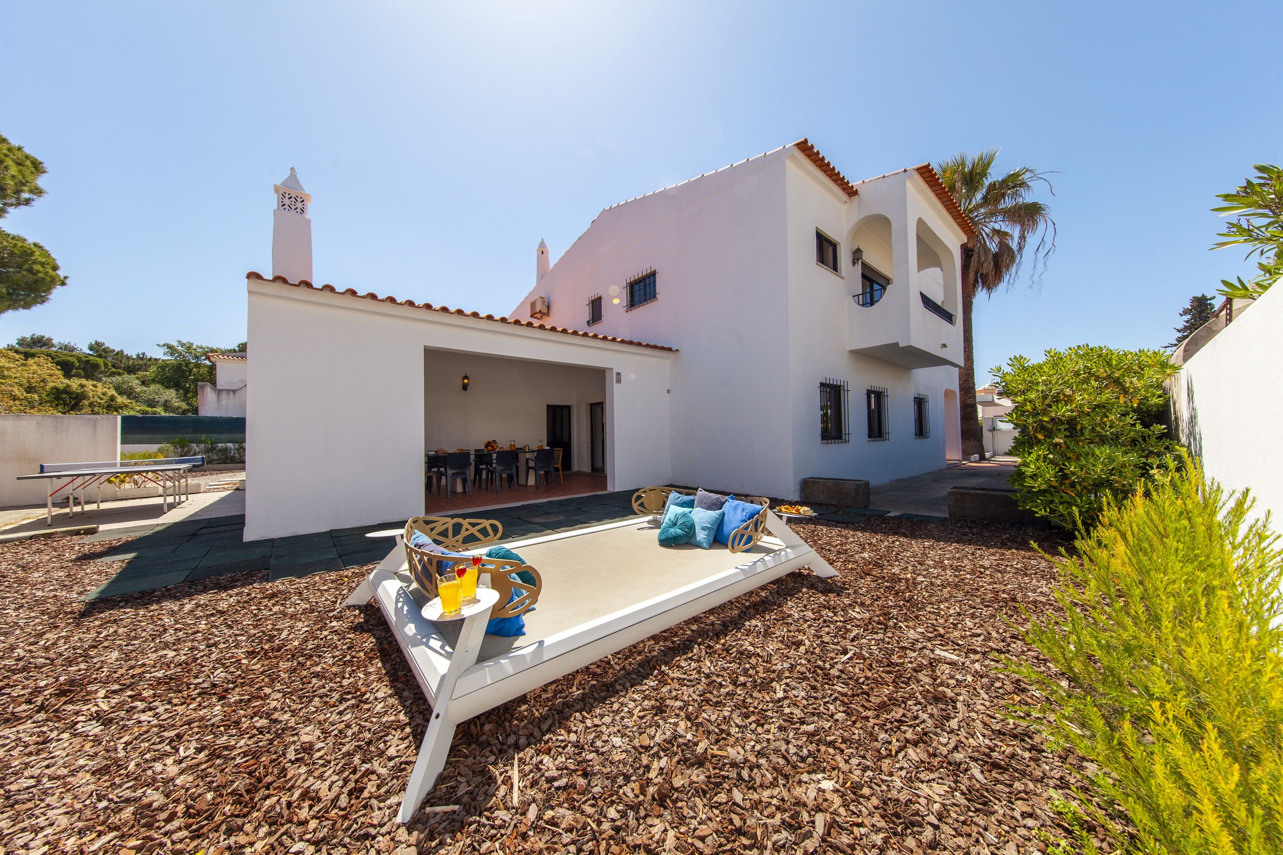 A white building with a covered patio area, outdoor seating, and a small pool.