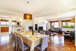 A spacious dining area with a large table set for six, surrounded by modern chairs. There is a television and a sofa in the living area, and large windows provide natural light. - Villa w/ Heatable Pool and BBQ in Albufeira (Albufeira)
