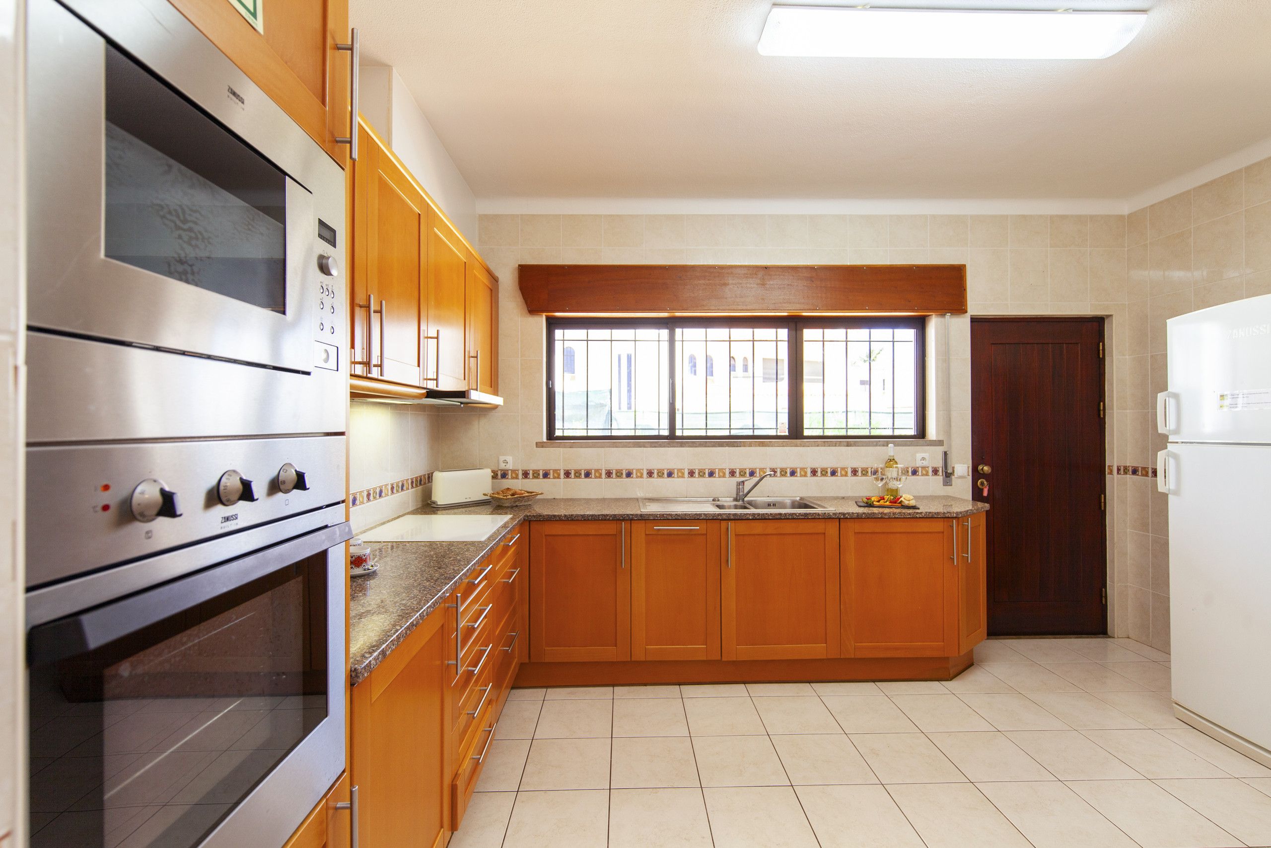 A kitchen with wooden cabinets, a built-in oven, a sink, and a window with bars.