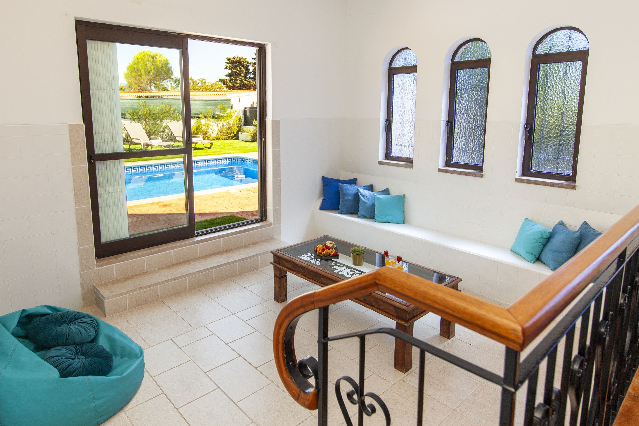 A living room with a pool view, a sofa with cushions, a coffee table, and a staircase.
