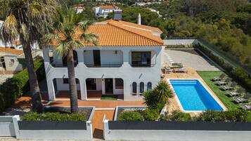 A two-story house with a swimming pool and sun loungers.