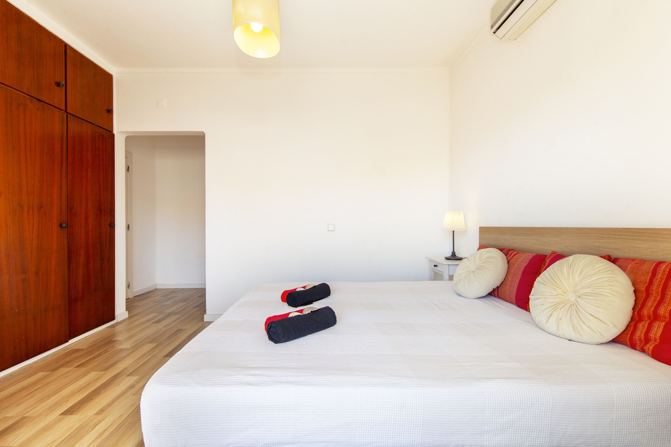 A hotel room with a wooden wardrobe, a bed with white bedding, and a nightstand with a lamp.