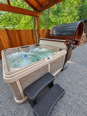 Ein Whirlpool mit einer Holzbank und einem Podest, umgeben von einem Holzzaun und Bäumen.