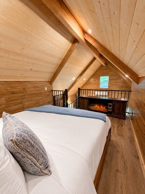 Ein gemütliches Zimmer mit Holzbalkendecke, einem Bett mit weißer Bettwäsche, einem Kamin und einem Fenster.