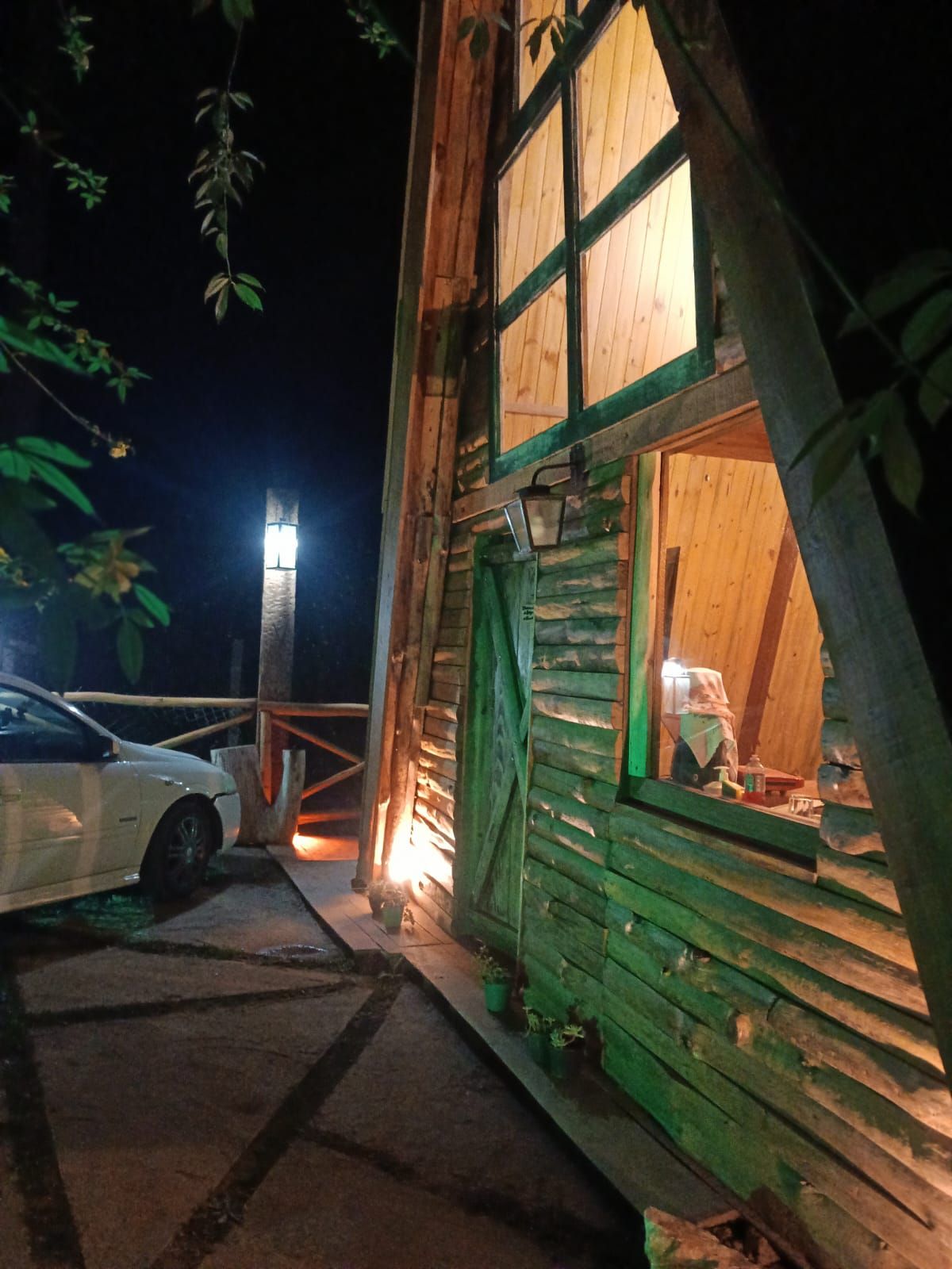 Uma cabana de madeira com um carro estacionado na frente, um deck de madeira e uma janela com moldura verde.