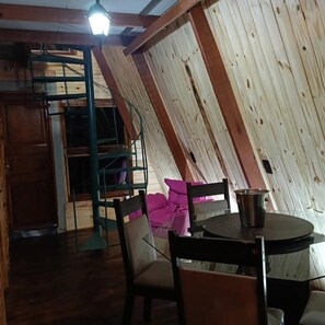 Um quarto com teto inclinado, uma mesa com cadeiras, uma panela de metal e uma escada.