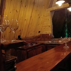 Interior em madeira com área de bar, copos e uma janela.