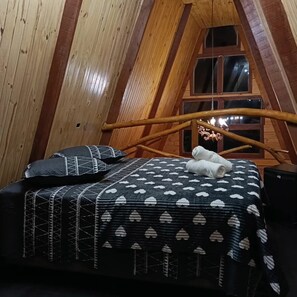 Quarto acolhedor com painéis de madeira, uma cama, almofadas e uma janela.