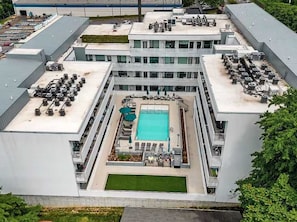 Un immeuble à plusieurs étages doté d’une piscine sur le toit, d’un espace extérieur aménagé pour s’asseoir et d’un grand espace ouvert.