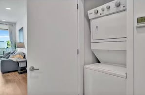 Une pièce moderne avec une grande fenêtre, un canapé gris, une petite table et un appareil électroménager blanc, peut-être un lave-linge ou un sèche-linge.