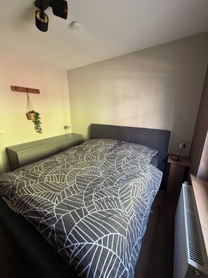 Une chambre à coucher comprenant un lit, une table de chevet, une étagère fixée au mur et un radiateur.
