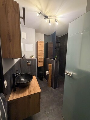 Une salle de bain moderne avec un meuble-lavabo en bois, un lavabo noir, un miroir et un espace douche.