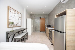 A compact kitchen with a refrigerator, stove, and sink. There's a bench and a table with a lamp. - Cozy Studio Steps from La Cerra (San Juan)