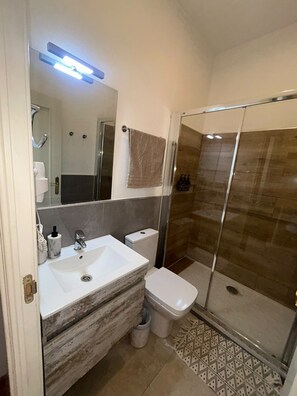 Ein Badezimmer mit Duschkabine aus Glas, einem weißen Waschbecken und einer Toilette.