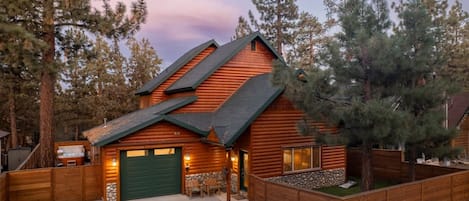 A log cabin with a green garage door, a stone foundation, and a wooden deck.