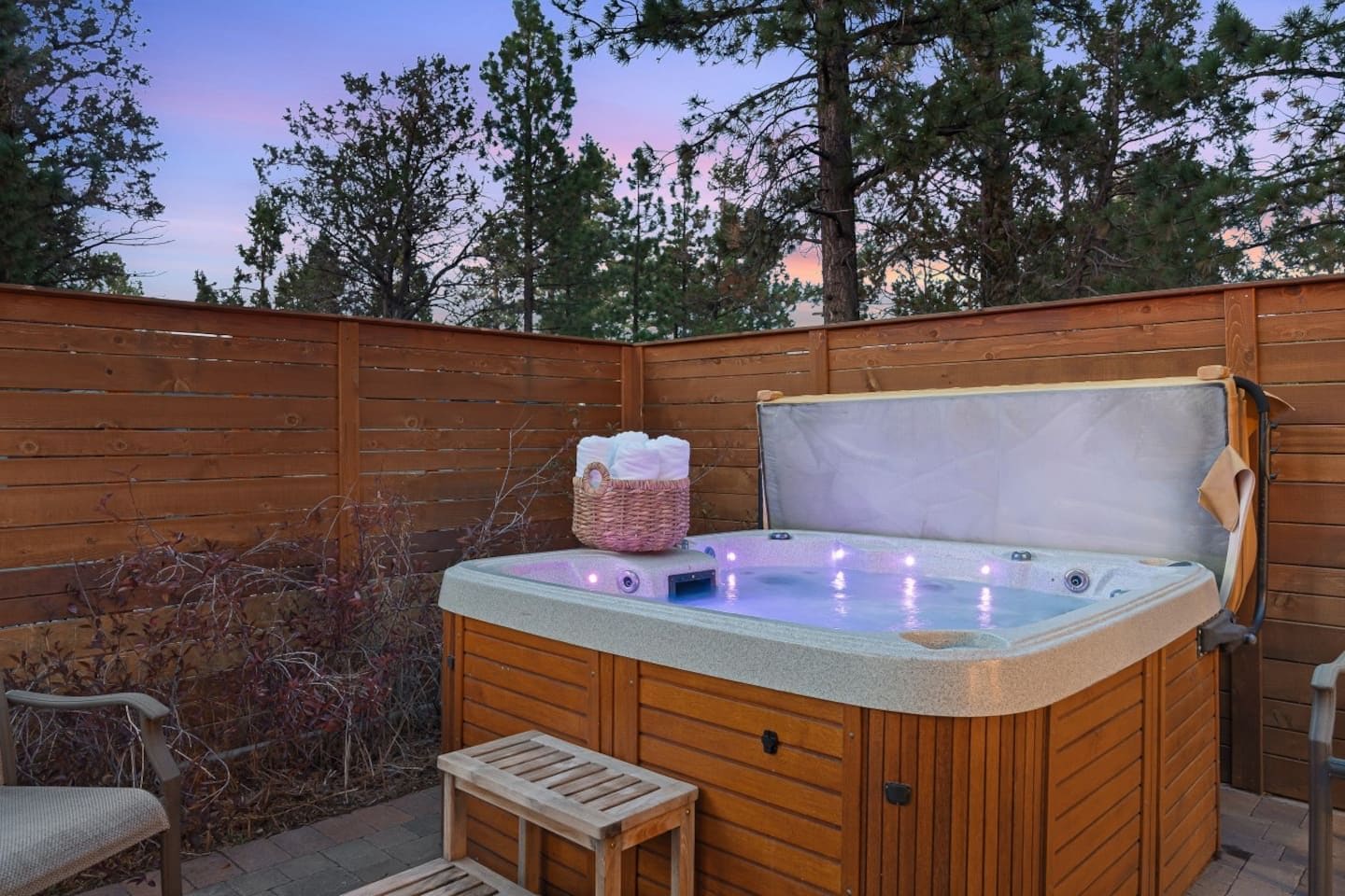 Un bain à remous avec une terrasse en bois, un panier en osier rempli de serviettes et un banc.