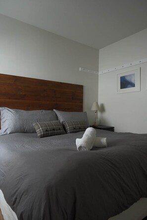 A neatly made bed with grey bedding and a wooden headboard. - Condo cosy ski-in/ski-out - village piétonnier (Mont-Tremblant)