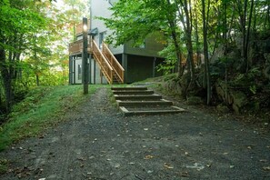 A pathway leading to a building with a wooden staircase and a deck. - Condo cosy ski-in/ski-out - village piétonnier (Mont-Tremblant)