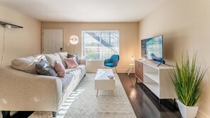 A living room with a sofa, coffee table, TV, and a plant. - Charming 2BR King Beds Suite Next to DT w Pool (Austin)