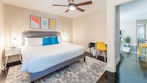 A bedroom with a bed, a ceiling fan, a nightstand, a chair, and a door leading to another room. - Charming 2BR King Beds Suite Next to DT w Pool (Austin)