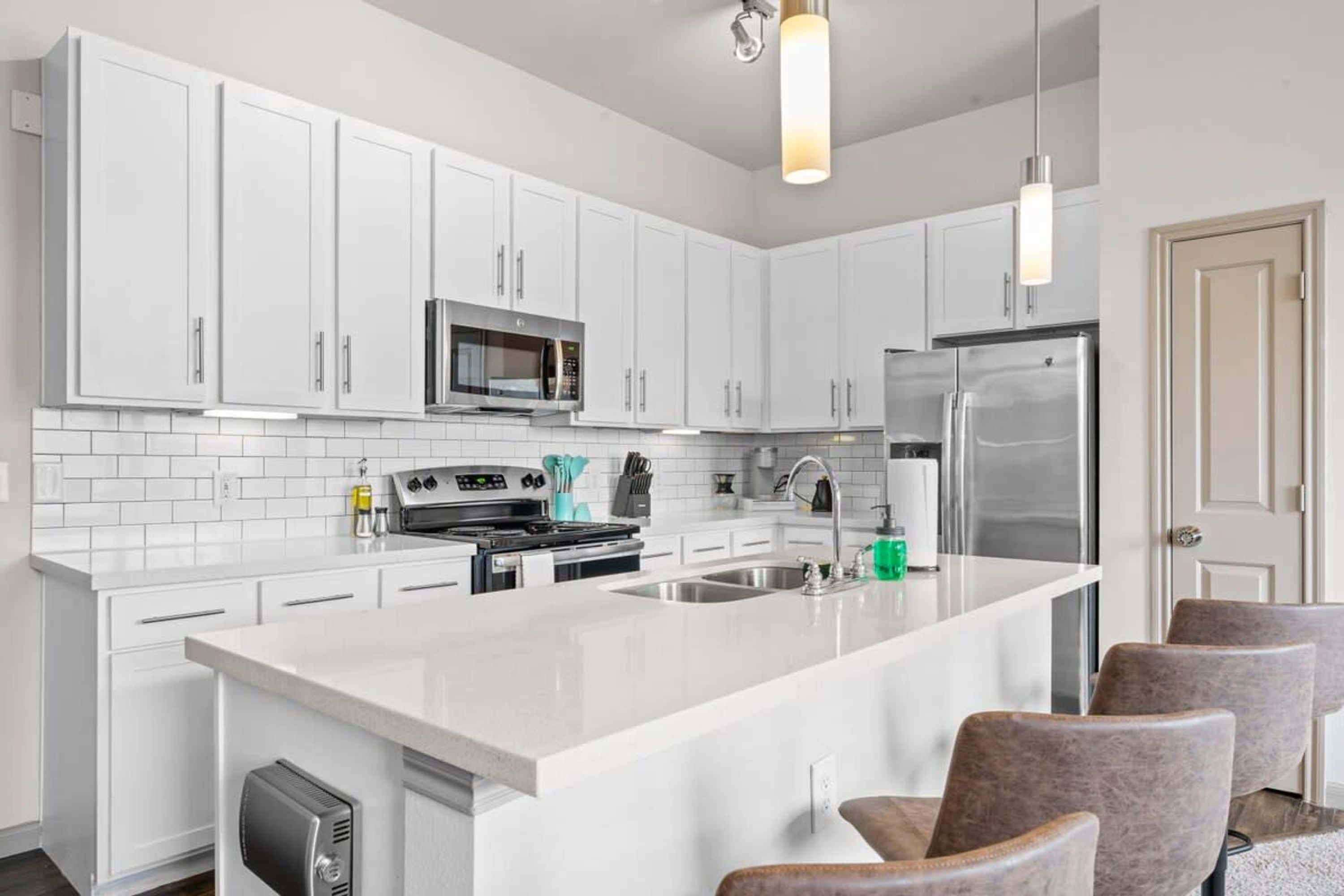 A modern kitchen with white cabinetry, stainless steel appliances, and a central island with seating.