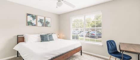 A bedroom with a bed, a desk, a chair, a ceiling fan, and a window with blinds.