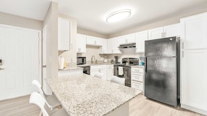 A modern kitchen with white cabinets, a granite countertop, a stainless steel refrigerator, and a built-in oven. - Bright 2BR King Suite w Gym Close to Downtown (Austin)