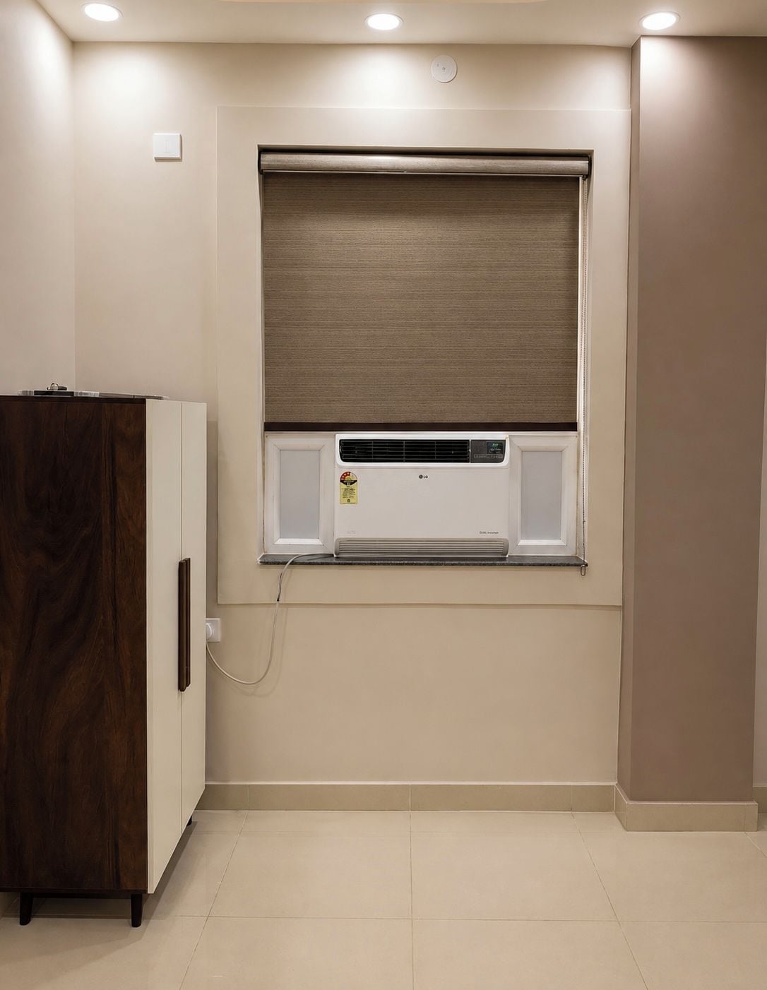 A room with a built-in air conditioner, a wooden cabinet, and a window with a blind.