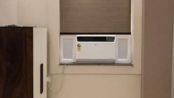 A room with a built-in air conditioner, a wooden cabinet, and a window with a blind.