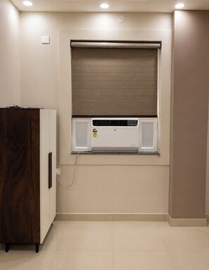 Una habitación con aire acondicionado integrado, un armario de madera y una ventana con persiana.