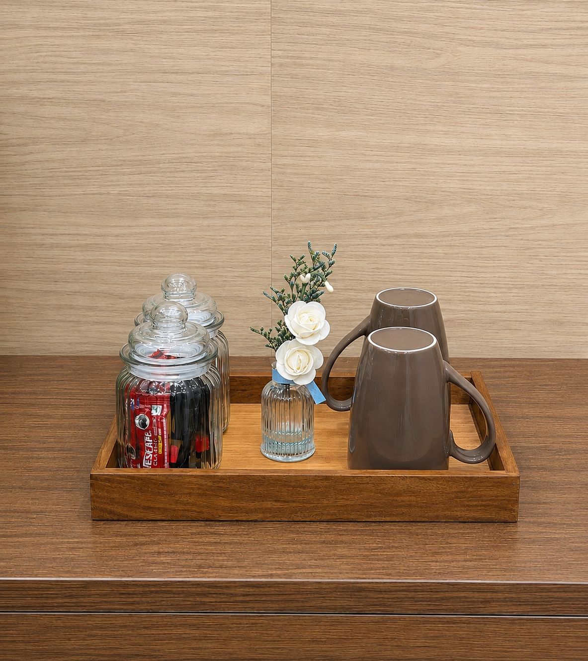 Ein Holzbahn mit einem Glasbehälter, einer kleinen Vase mit weißen Blumen und einer braunen Tasse.