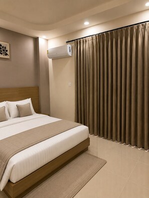 Ein Hotelzimmer mit einem großen Bett, einem Kopfteil, einer Wand-Klimaanlage und einem fenster mit Vorhängen.