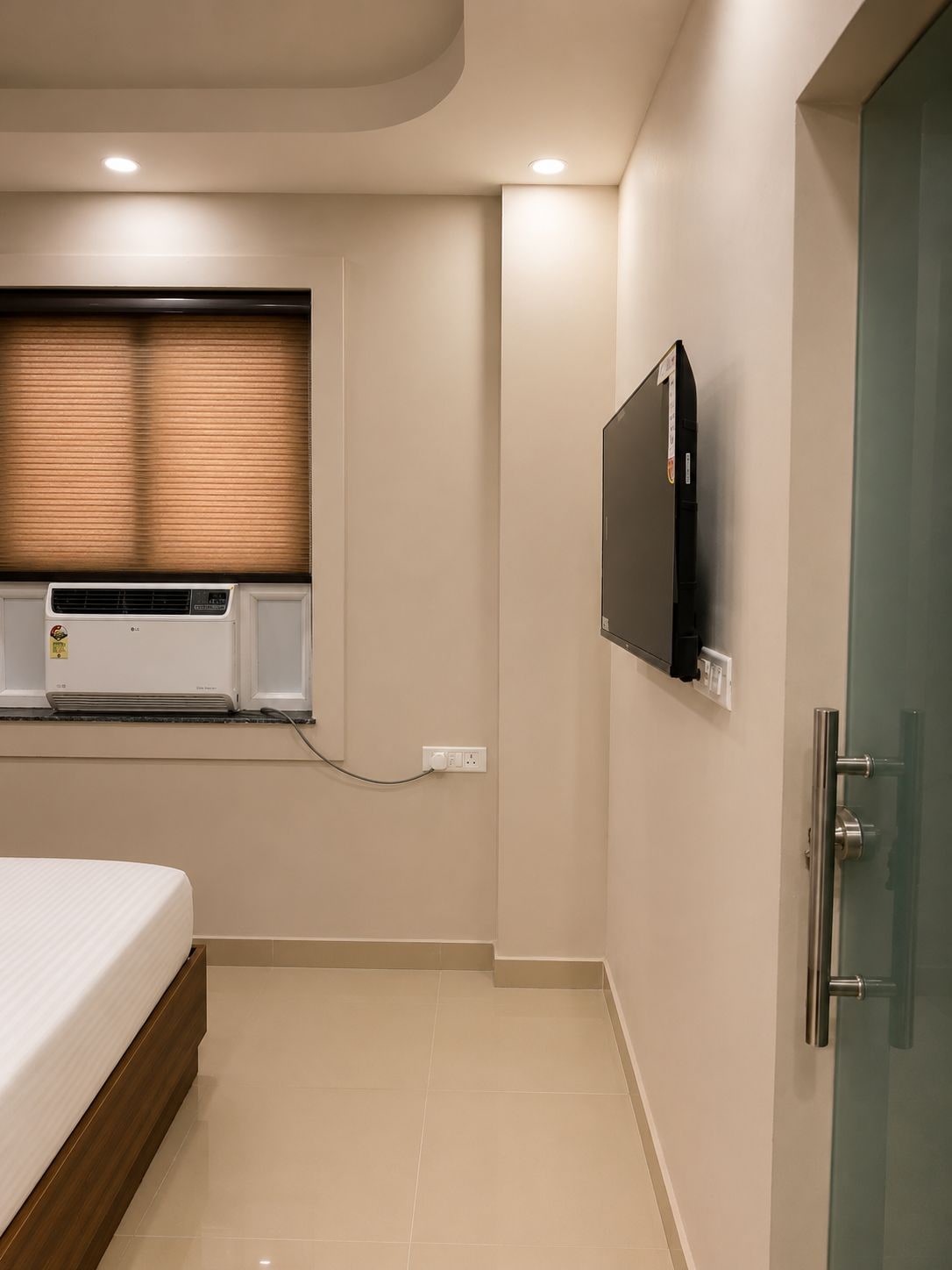 Een slaapkamer met een bed, een wandtelevisie, een airconditioning en een deur met een ruit.