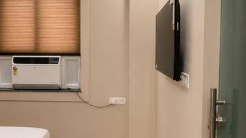 Een slaapkamer met een bed, een wandtelevisie, een airconditioning en een deur met een ruit.