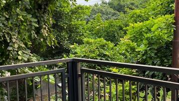 A balcony with a metal railing overlooking a garden with various trees and shrubs.