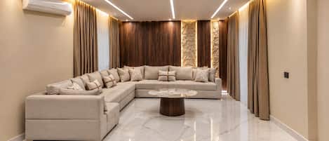 A modern living room with a sectional sofa, a round coffee table, and a wall-mounted air conditioning unit.