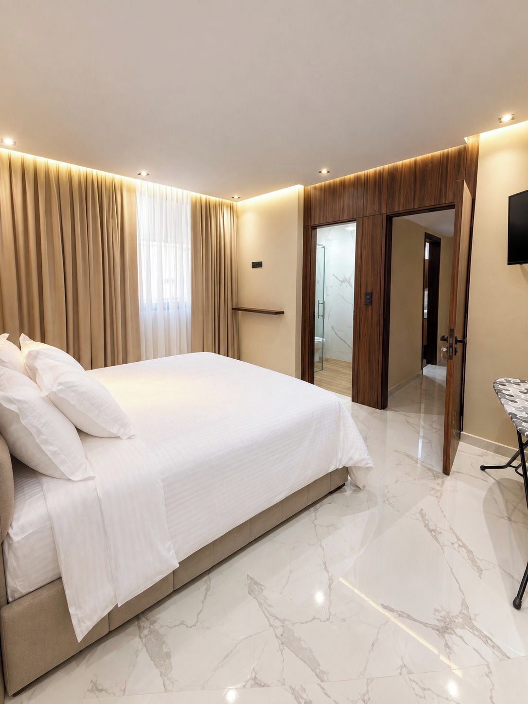 Een moderne slaapkamer met een groot bed, een inloopkast en een flatscreen televisie aan de muur.