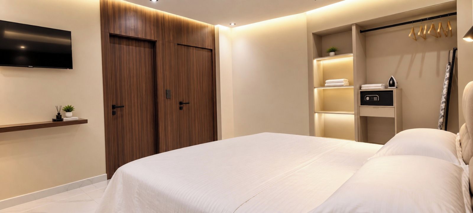 Une chambre à coucher moderne avec un grand lit, un téléviseur fixé au mur et une armoire avec un miroir.