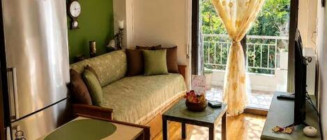 Una sala de estar con sofá, una mesa de centro, televisor y ventana con cortinas.