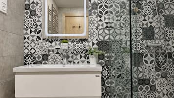 A bathroom with a white vanity, a mirror, and a shower area with patterned tiles.