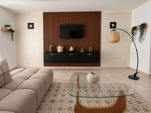 Un salon moderne avec un canapé, une table basse en verre, un téléviseur fixé sur un mur recouvert de panneaux en bois et une lampe sur pied.